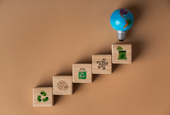 Blocos de madeira organizados em formato de degraus de escada, com desenhos representando sustentabilidade, e uma lâmpada desenhada com detalhes do globo terrestre no topo, representando MBA em ESG.