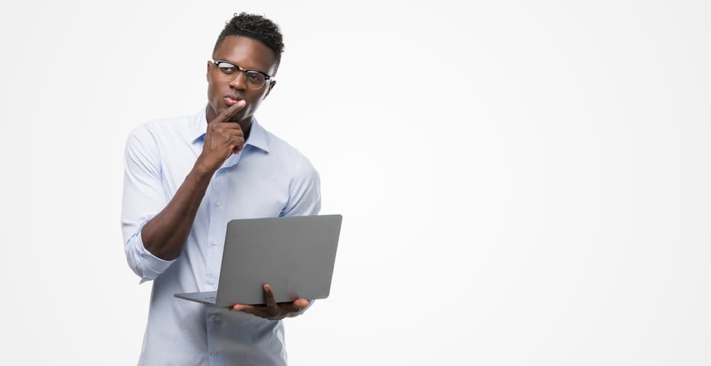 Homem segurando notebook e fazendo expressão de pensativo, representando o pensamento crítico.