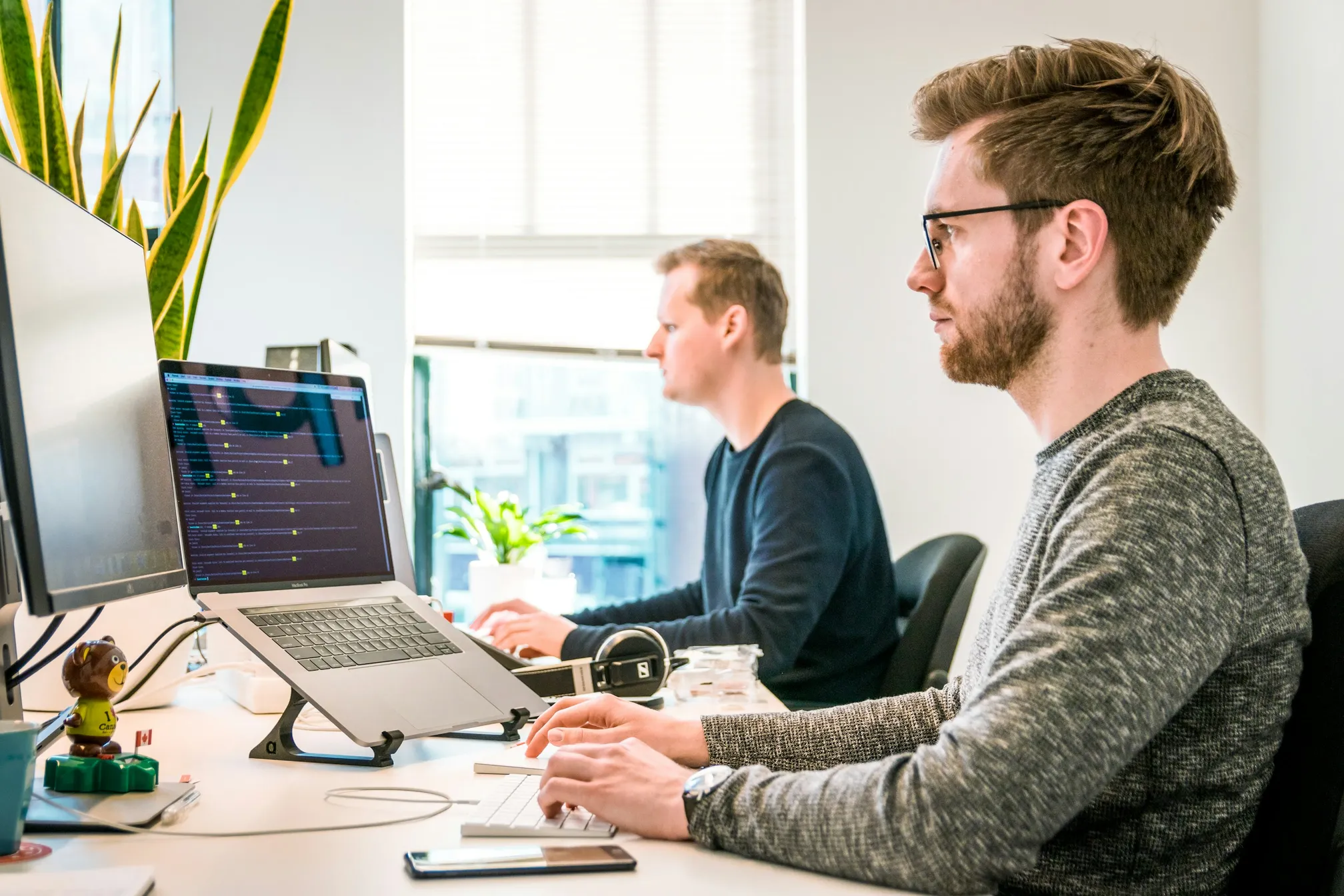 Dois profissionais programando lado a lado em um escritório, com código na tela do notebook